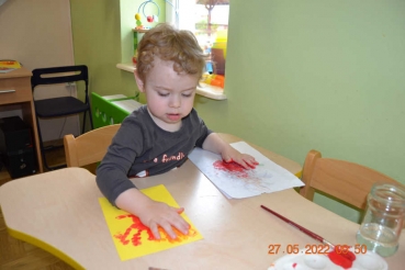 Chłopczyk odbija rękę na kartce papieru czerwoną farbą